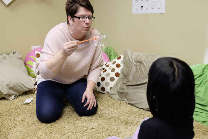 Woman in playroom blowing bubbles playing with adopted child sitting facing her