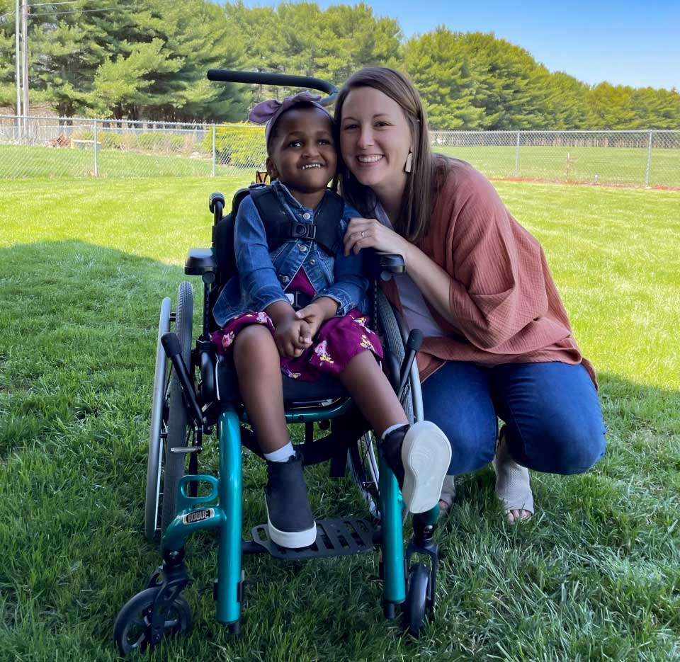 woman smiling beside girl in wheelchair