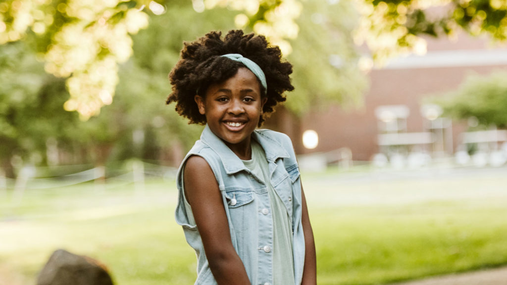 smiling girl with natural hair in a blue headband and denim vest adopted from ethiopia