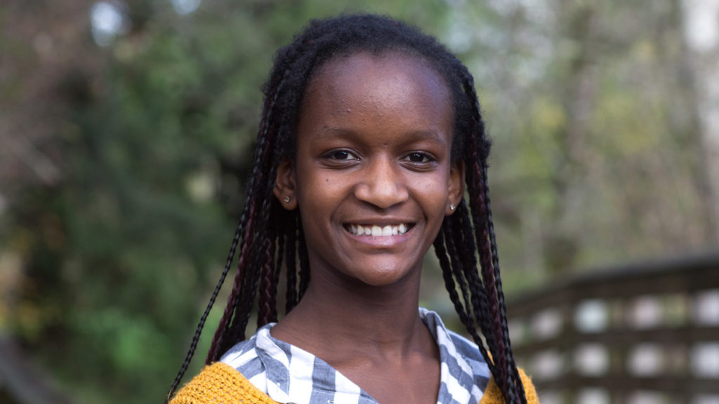 smiling girl with yellow sweater and hair in braids adopted from uganda