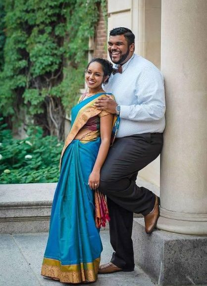 smiling woman in turquoise sari leaning on laughing man in dress clothes
