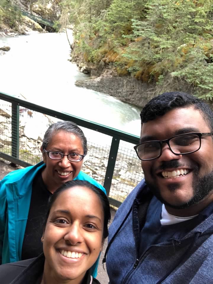 three smiling adults in front of a small waterfall