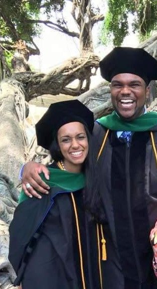 smiling man and woman wearing graduation gowns, master's capes and doctoral caps