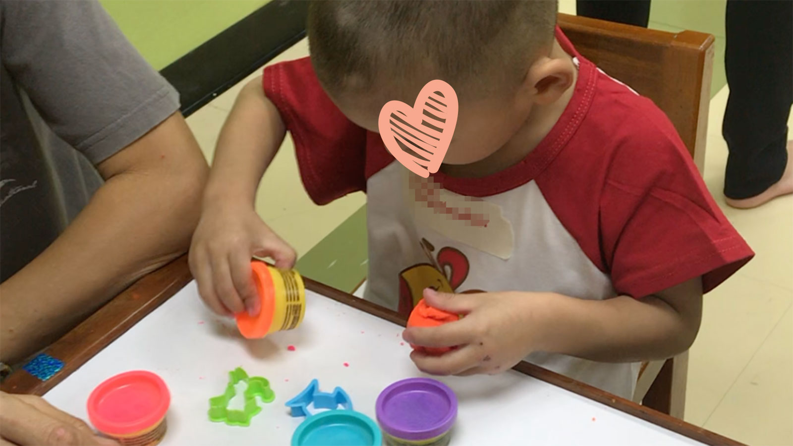 little boy playing with playdough with heart graphic covering his face