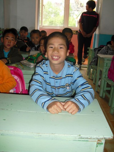 Smiling boy in blue striped shirt sitting at a desk in a classroom in China