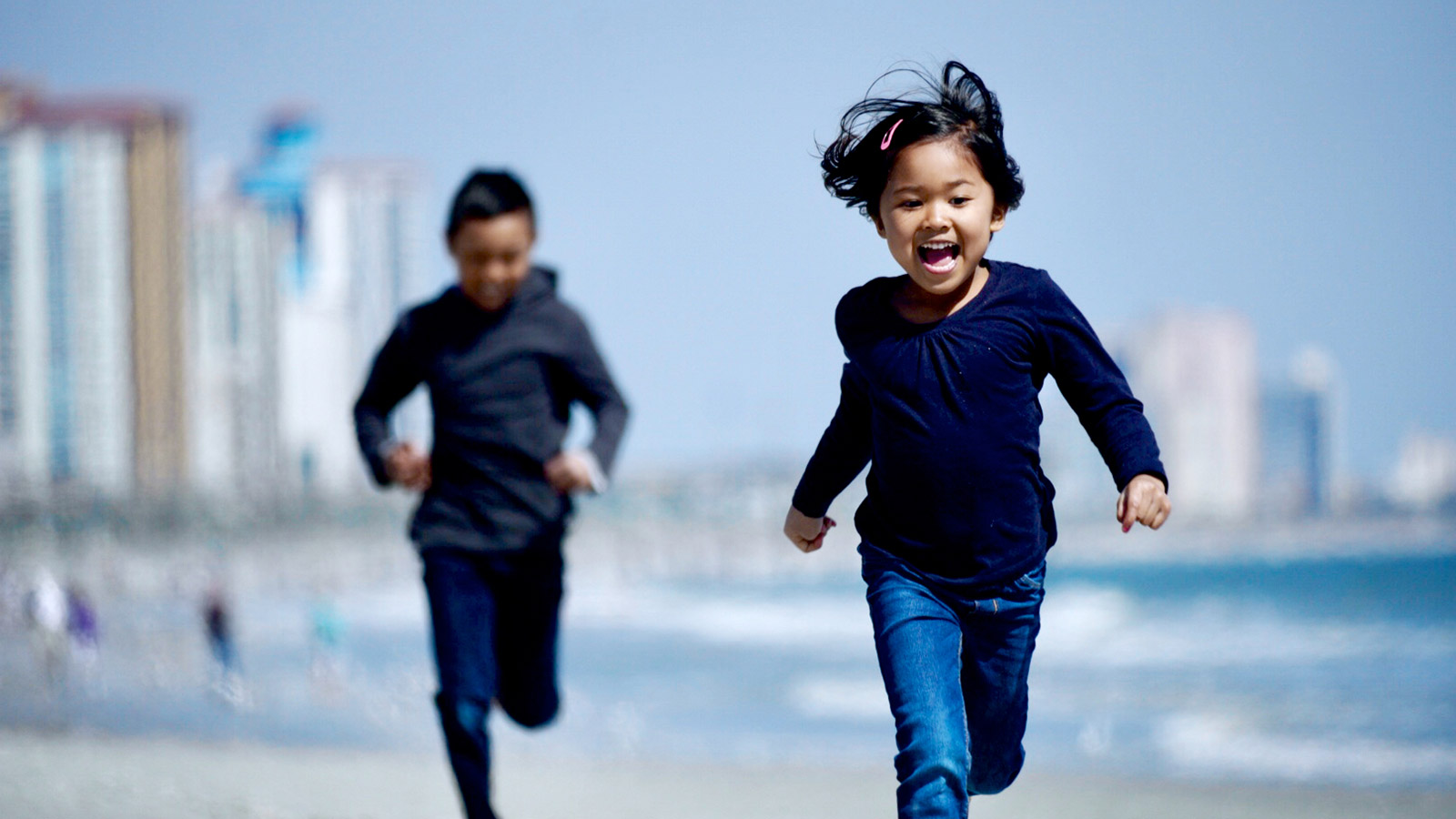 two siblings running together and laughing on the beach