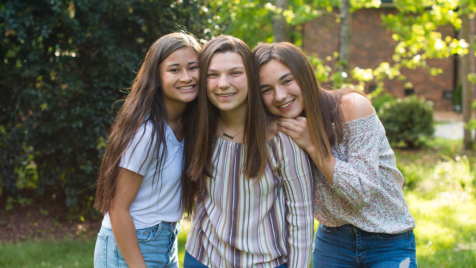 three sisters one adopted from Thailand smiling with arms around each other