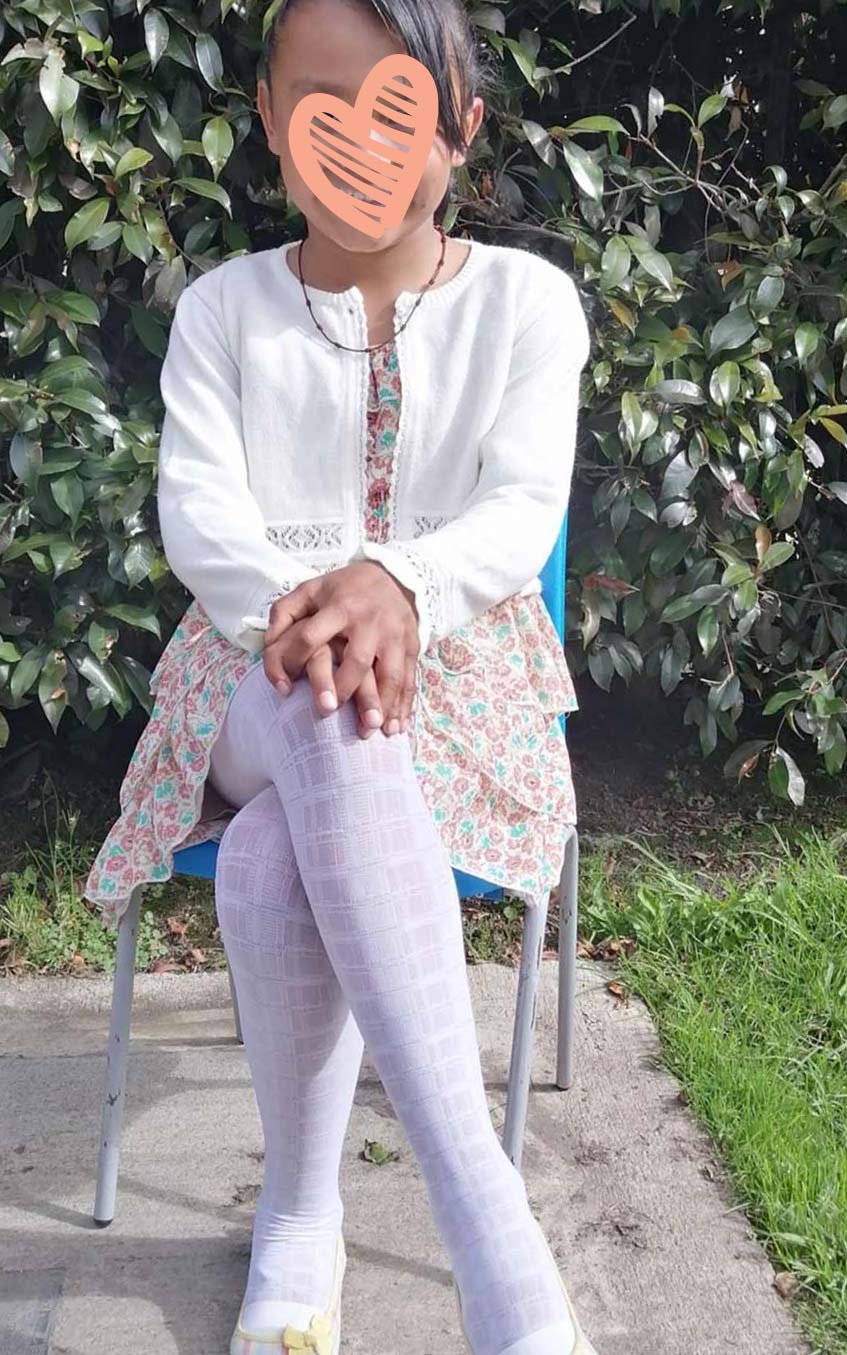 little girl wearing white sweater and flowered dress sitting in chair with heart graphic over face