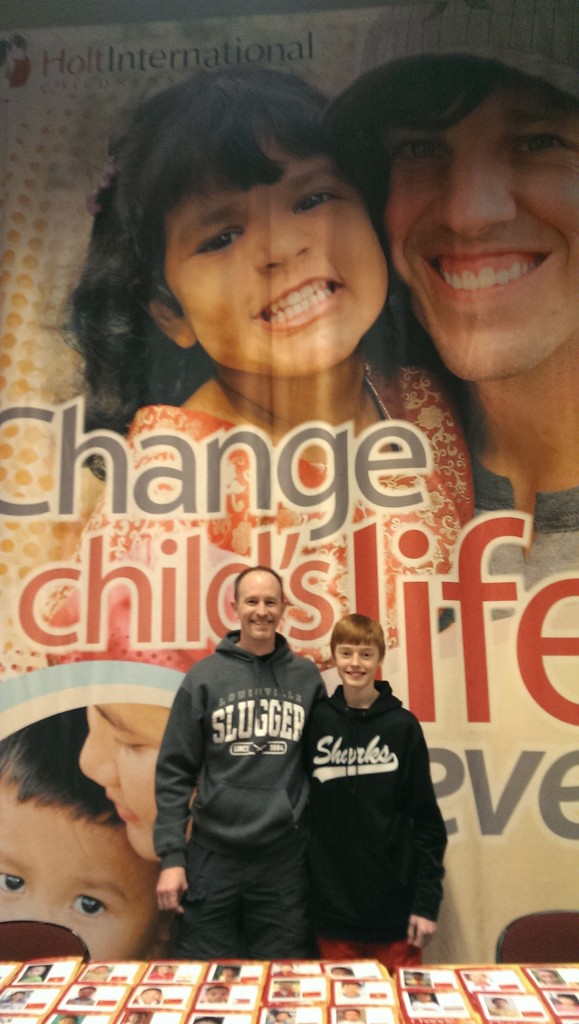 Greg stands in front of the Holt banner with his son at a Winter Jam concert in Ohio. Greg's daughter, a Holt adoptee from India, is featured on the banner with NewSong band member Matt Butler, which came as a surprise to Greg.