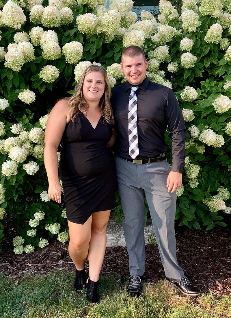 smiling man and woman in formal wear in front of white flowers