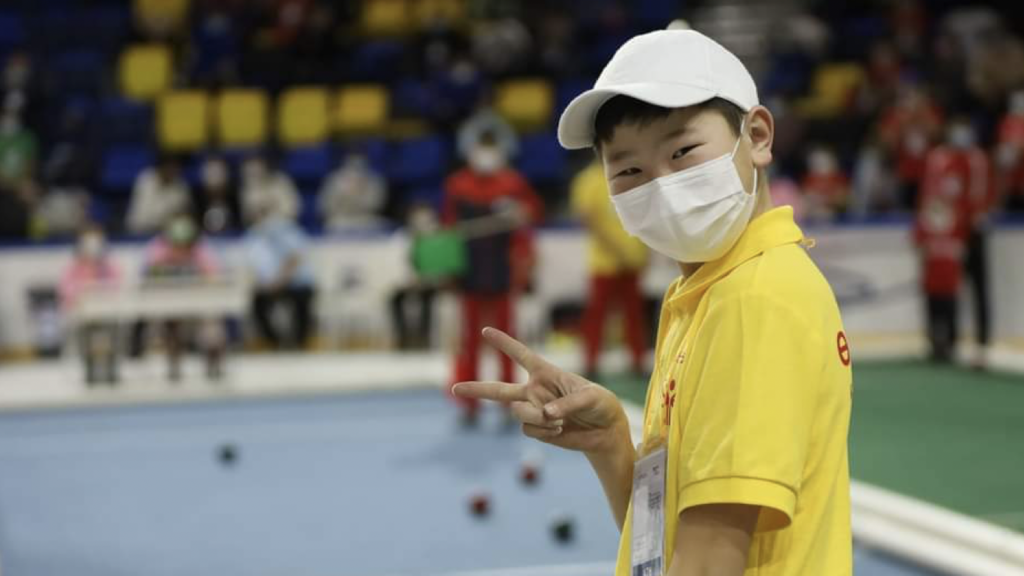 A boy plays bocce ball and smiles at the camera