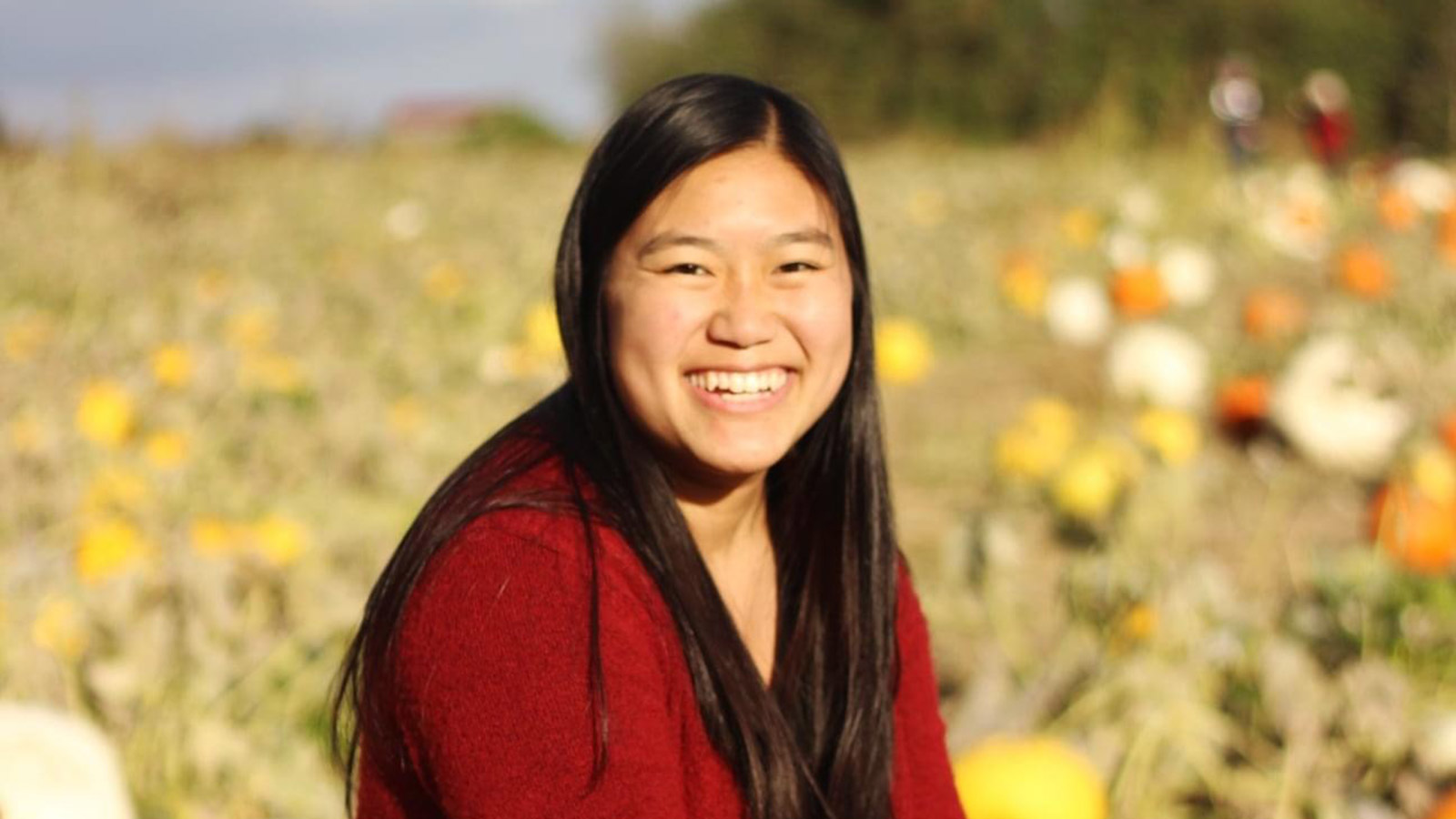 smiling adult adoptee from china sitting in pumpkin patch