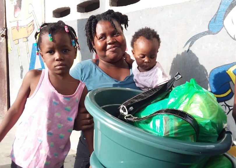 A mom and two young children in Haiti pose with their kit of emergency food and supplies. 