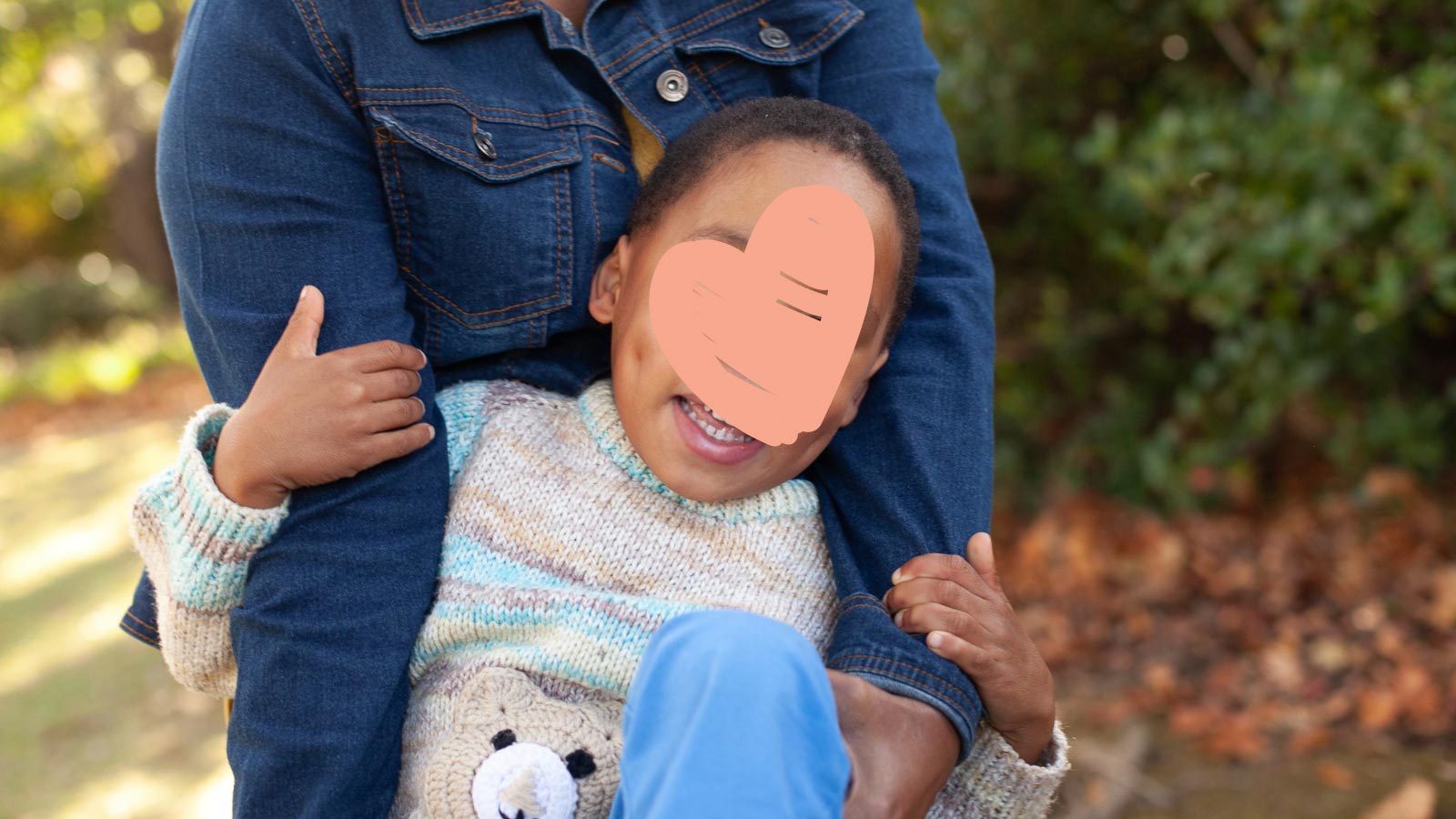 little boy with heart graphic covering face being held by his caregiver