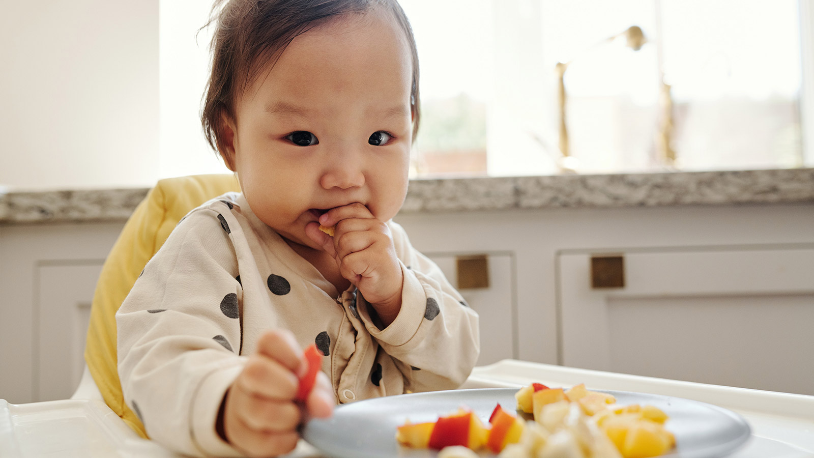 baby girl eating a piece of fruit