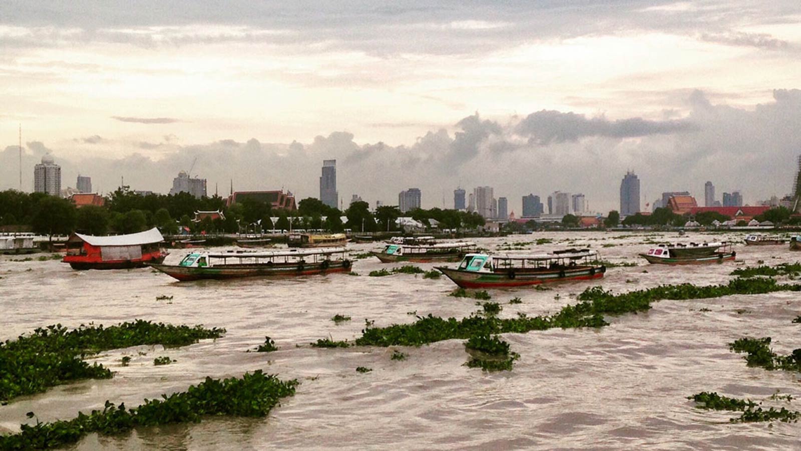 Boats in city harbor in Thailand in front of gray, cloudy sky