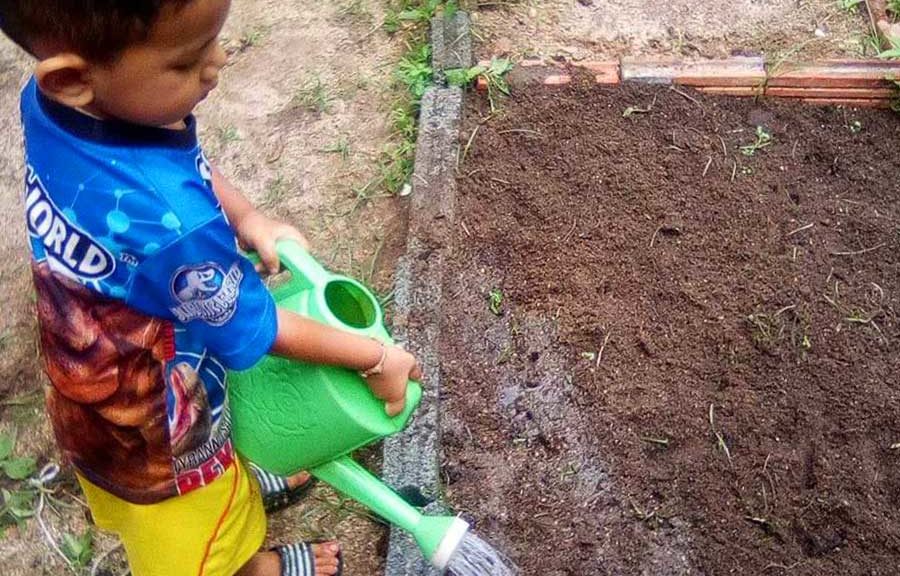 little boy uses a watering can in his garden