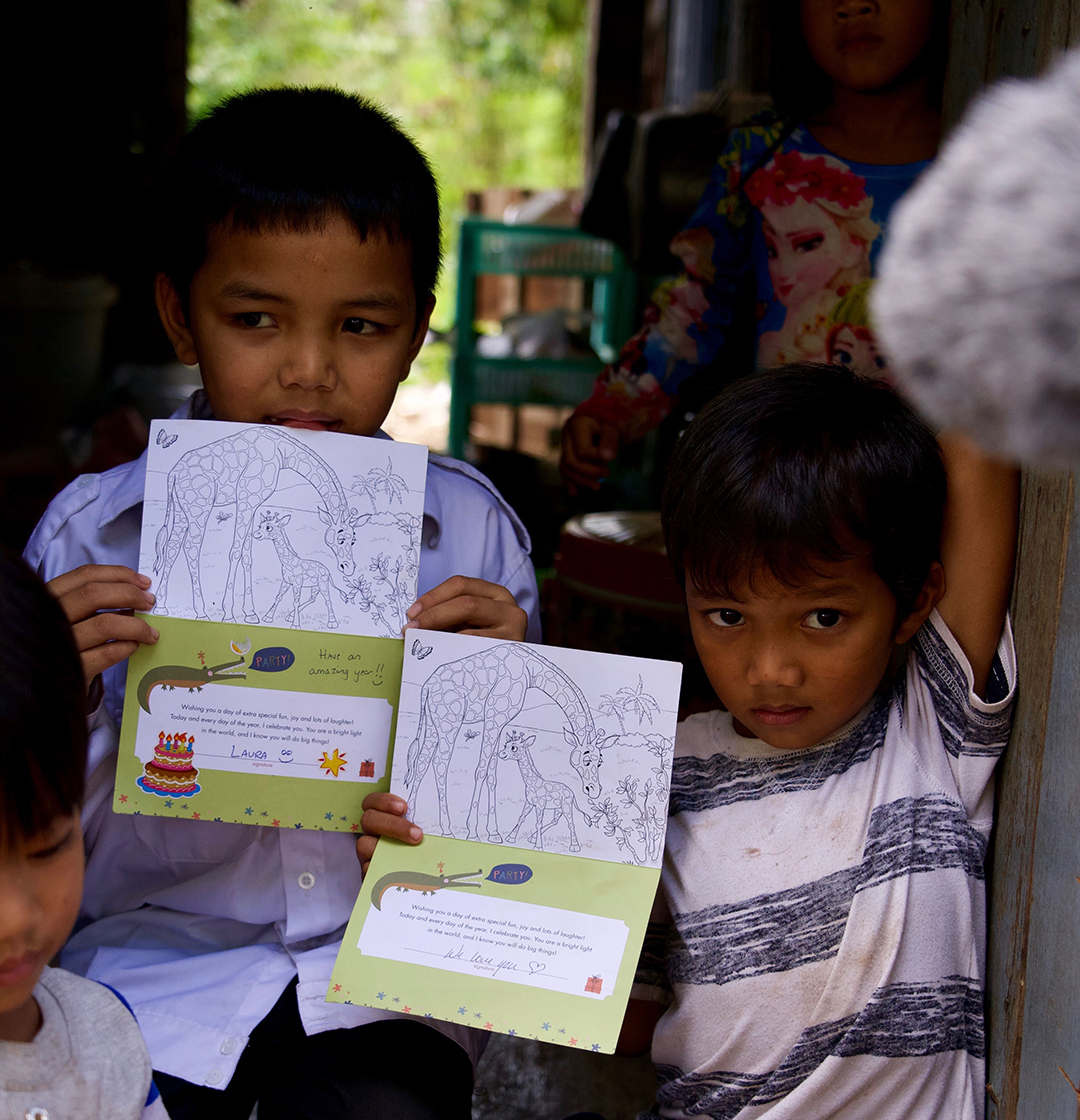 Two boys in Cambodia hold up birthday cards that were signed by Holt staff