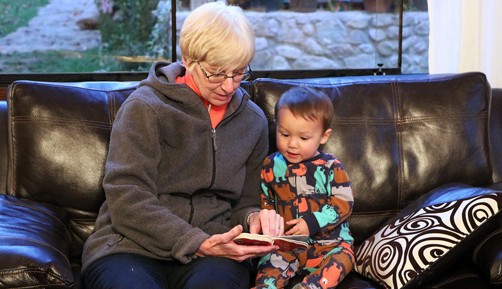 older woman reading book to smiling toddler boy