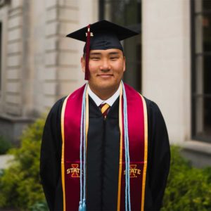 smiling man wearing black graduation cap and gown and red sash