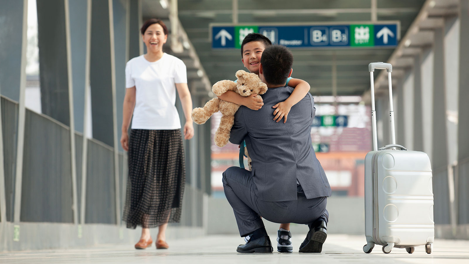 child holding teddy bear running to embrace father in airport