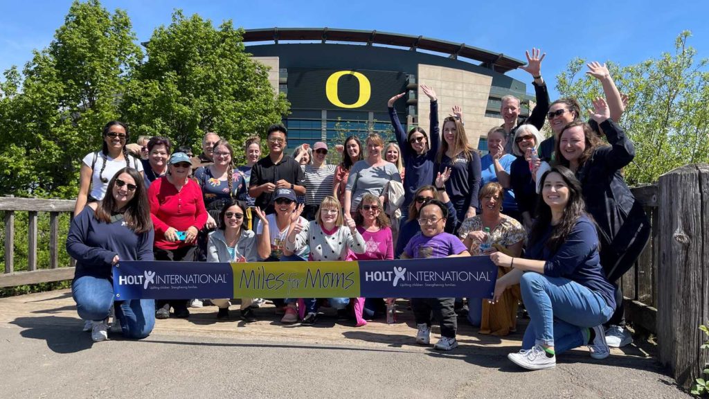 A group celebrates in front of football stadium with "Miles for Moms" banner