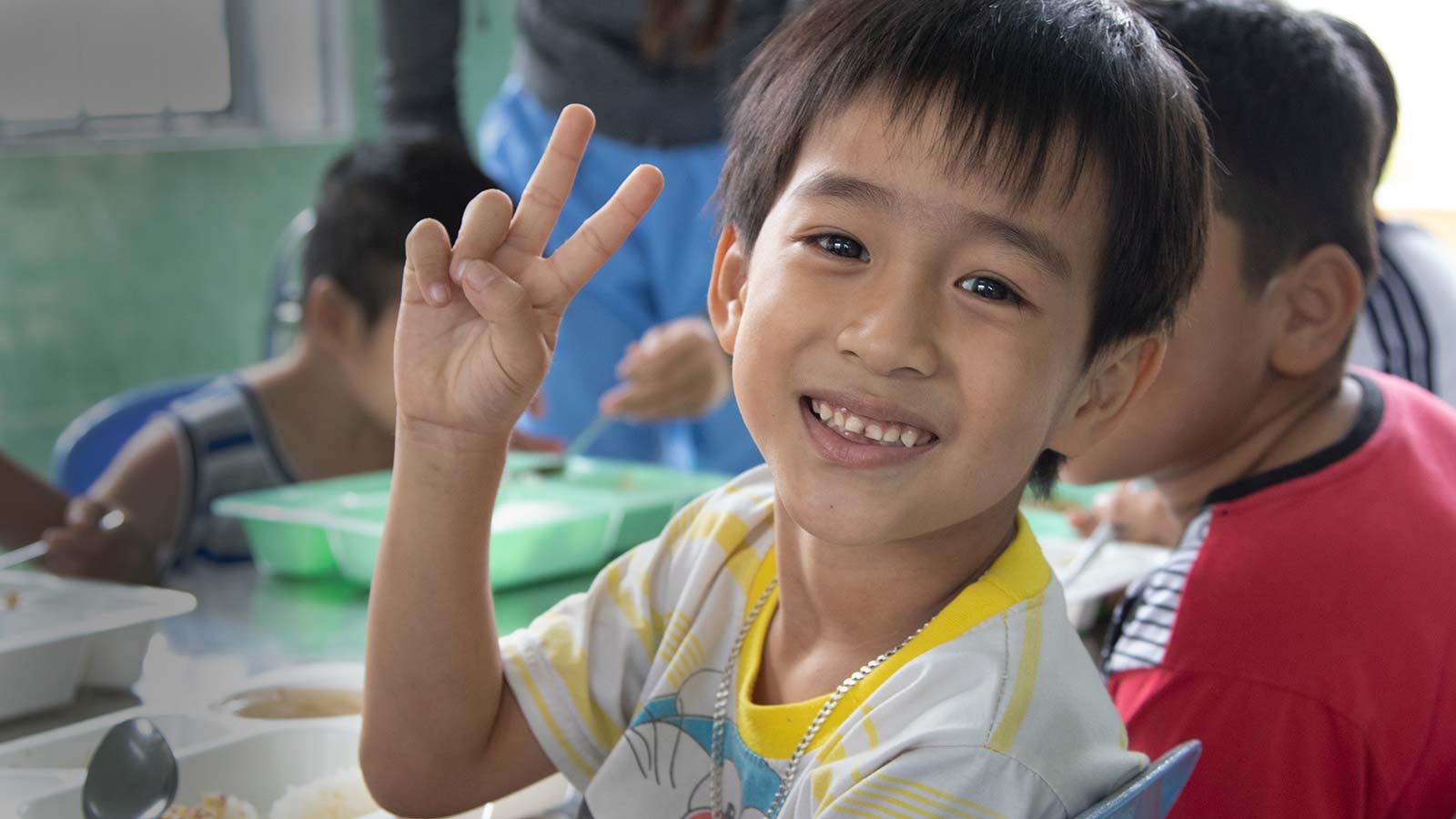 Vietnam boy giving peace sign while eating with fellow children in need of sponsorship support