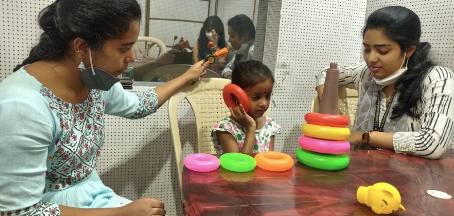 A girl holds a plastic ring toy up to her ear