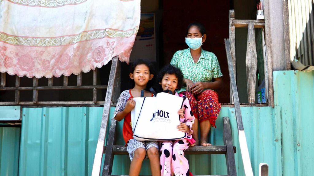 Sponsored children in Cambodia with their grandma, holding a Holt International bag full of gifts