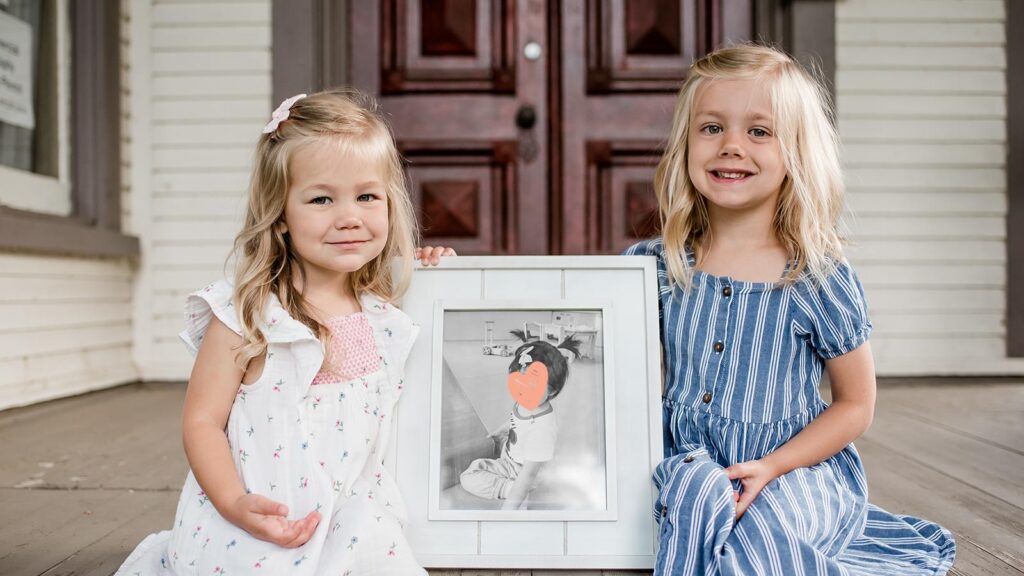 sisters posing with photo of future adopted sister with help of snaf grant