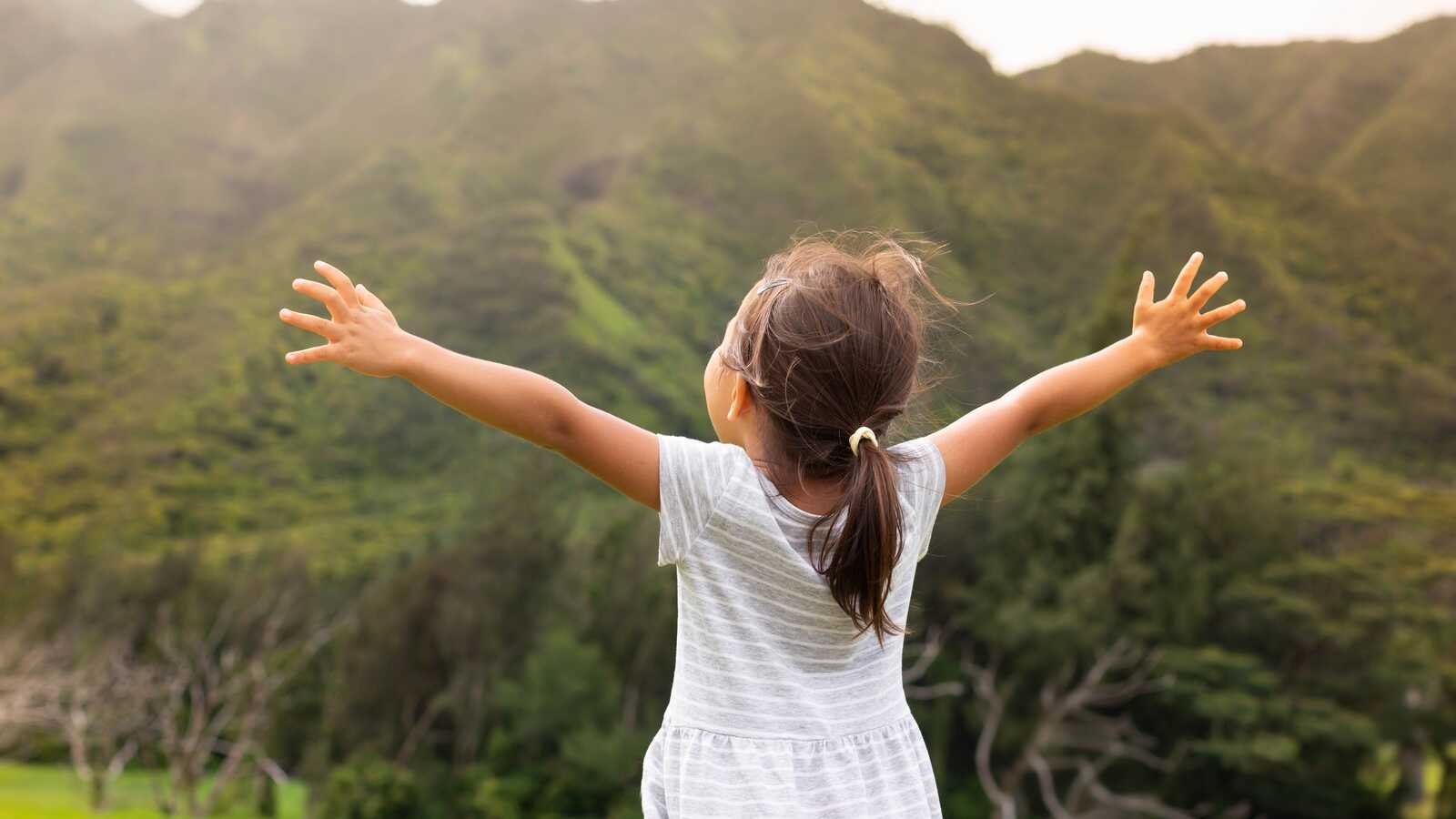 china, little girl with arms outstretched looking at mountains in front of her