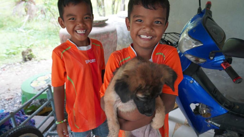 Sponsored twin brothers holding a puppy at home in Thailand