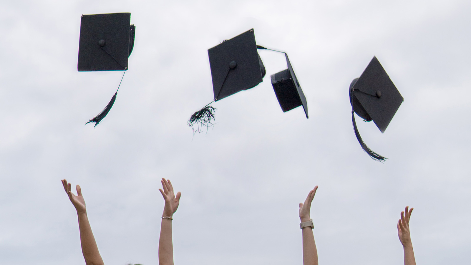 four people throwing graduation caps into the air