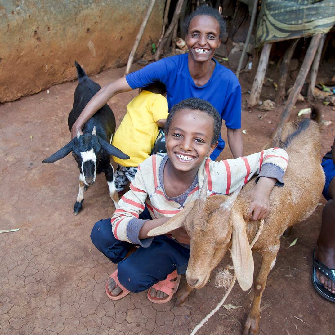 A boy and his mom post with goats outside their home in Ethiopia