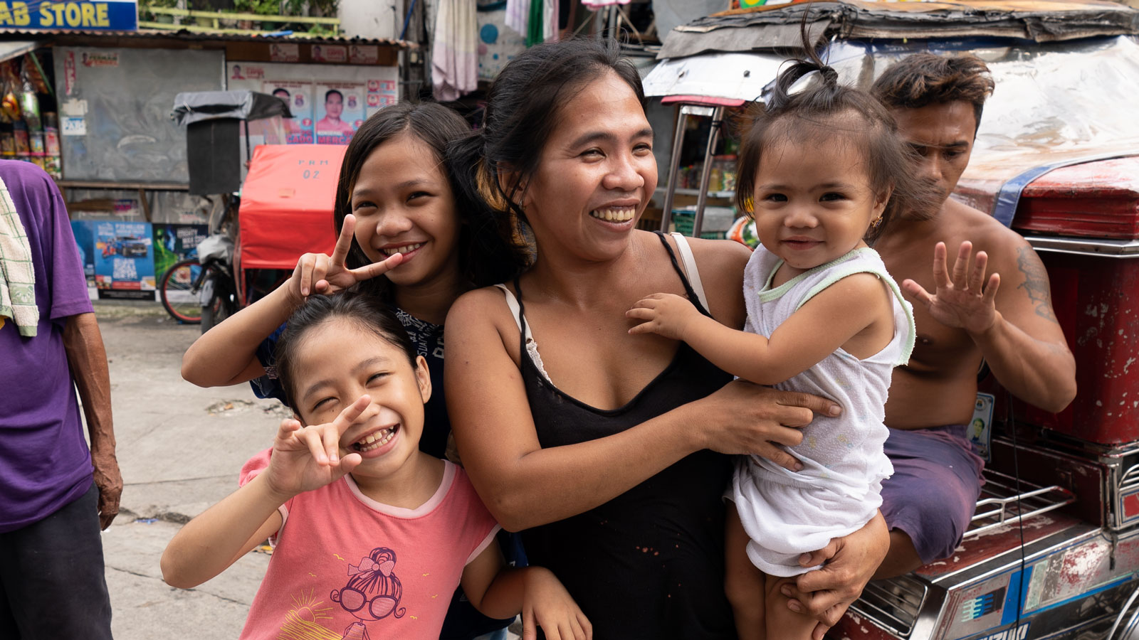 A mom and her daughters in the Philippines smiles outside their home