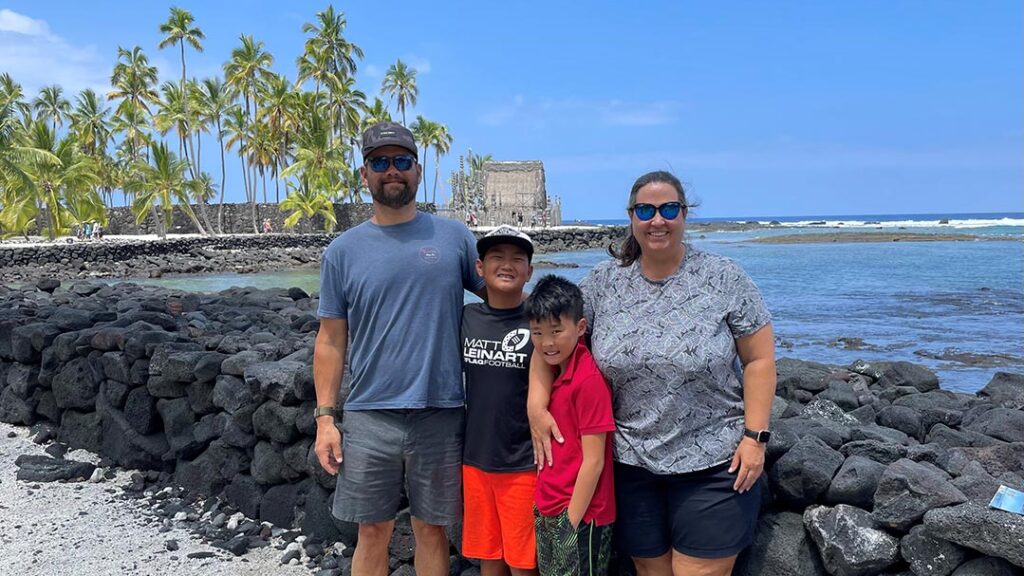 adoptive family with two boys stand and smile on the beach