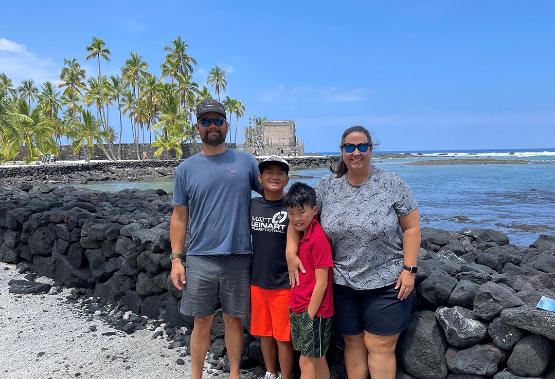 adoptive family with two boys stand and smile on the beach