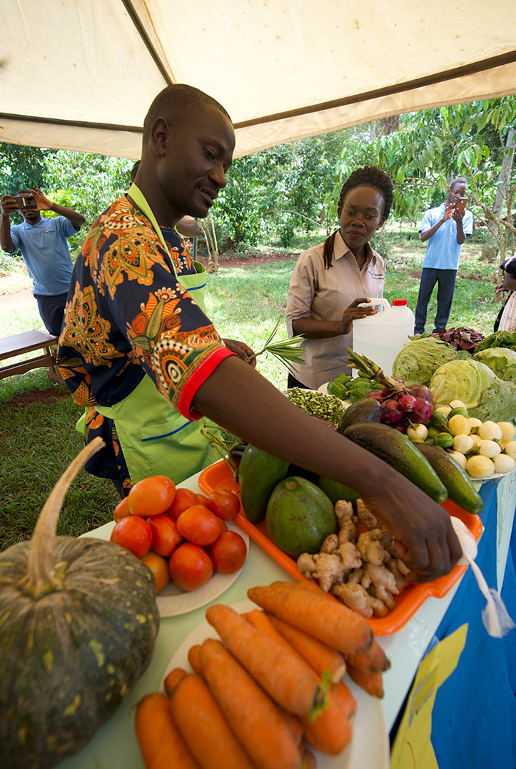 a health worker shows ginger and other vegetables to parents