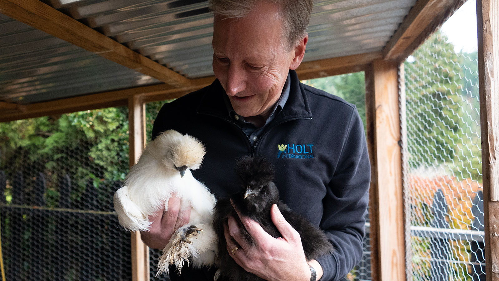 A man looks down at two chickens he is holding