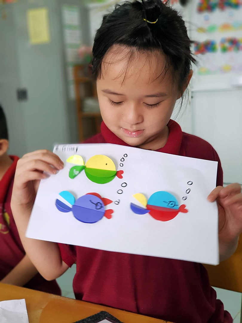 A girl holds up an art project of fish made out of paper