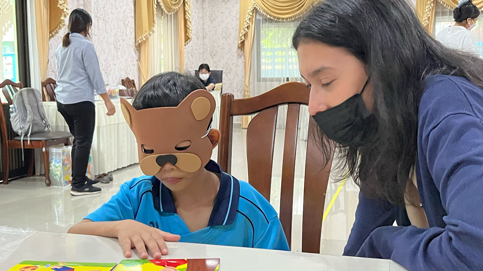 Little girl wearing animal mask sitting at table playing