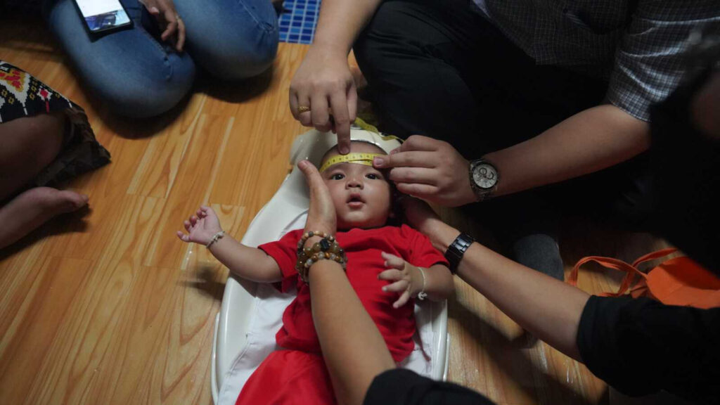 A boy in a Burmese migrant community in Thailand has his head circumference taken