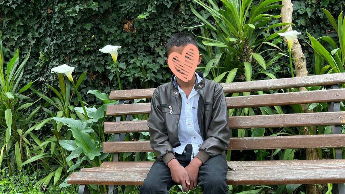 Young boy sits on park bench with face covered