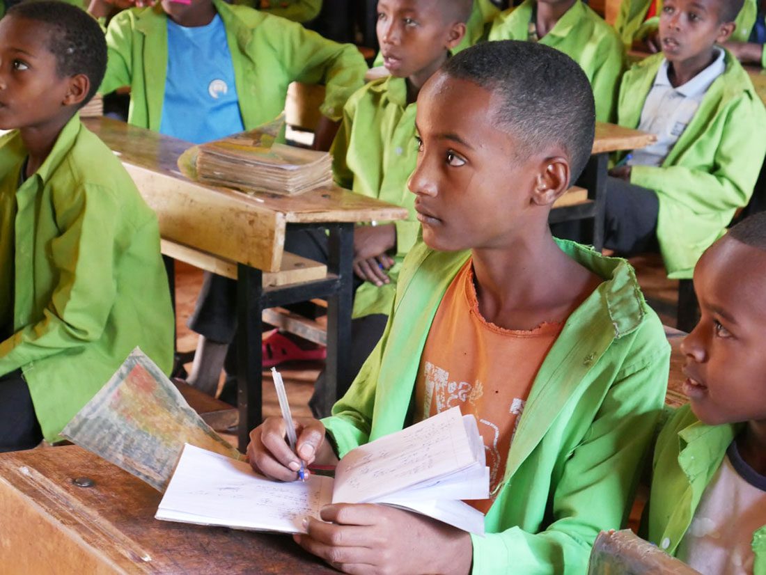 Young boy studies in classroom with other students.