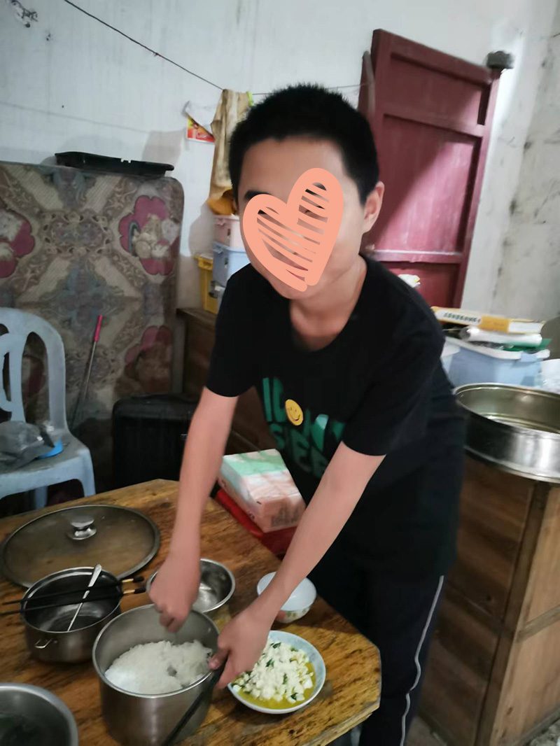 Boy stirs rice at the dinner table while looking into camera