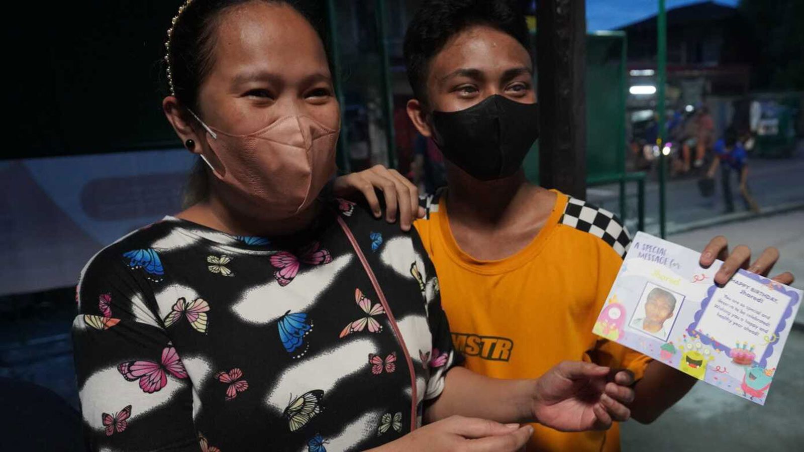 Gabriel, a boy in educational sponsorship in the Philippines, holds a birthday card from his sponsor as he stands by his mom.