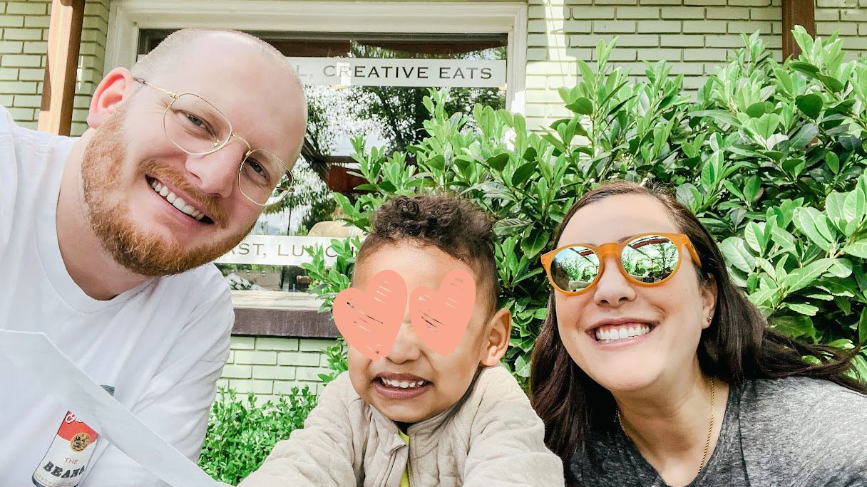 Parents and toddler smile together in front of shop