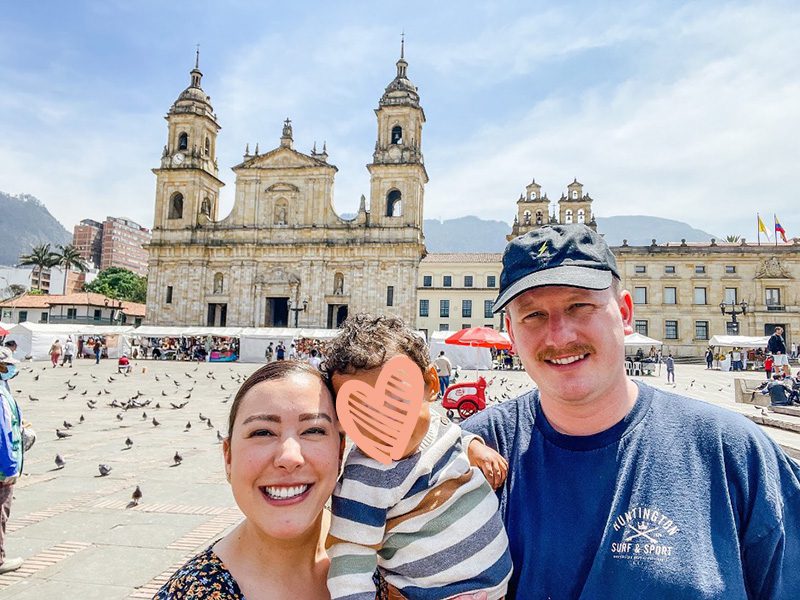 Parents and toddler smile together outside ornate public building in Colombia