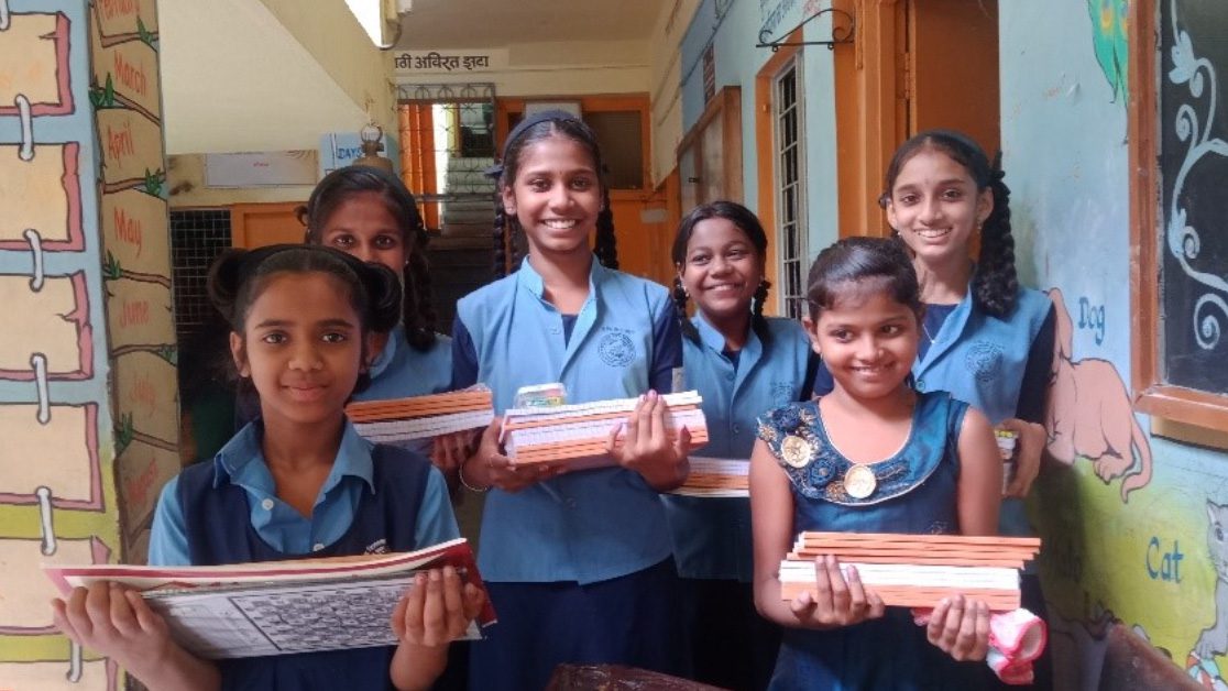 Smiling girls in school uniforms hold new books in India