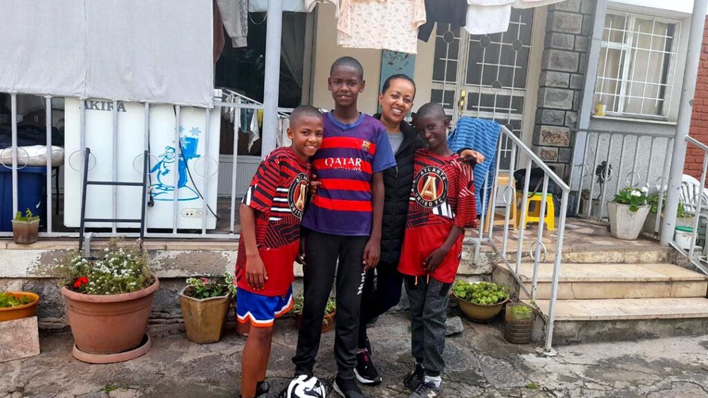 three boy post with their foster mom in front of their house in Ethiopia